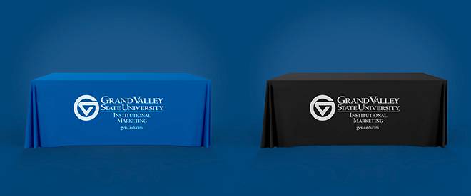 A table with a blue throw on it adjacent to a table with a black throw on it. Both throws have a white Grand Valley Institutional Marketing logo on them.